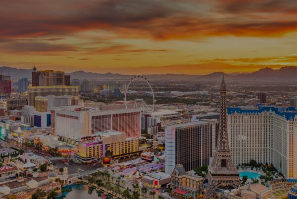 A panoramic view of the Las Vegas Strip at sunset, featuring brightly lit hotels, casinos, the High Roller Ferris wheel, and an orange sky with mountains—showcasing one of the cheapest LAX destinations for a vibrant getaway.