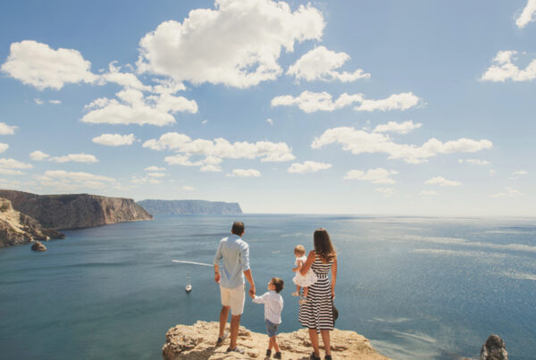 A family of four stands on a cliff overlooking a vast, blue sea and rugged coastline under a partly cloudy sky, making the most of their sunny day and showing how to maximize your PTO with breathtaking views.