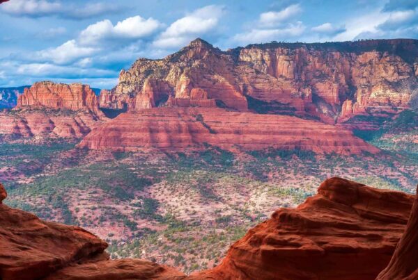 View of red rock formations and mesas under a partly cloudy sky, seen through the opening of a cave or rock arch in Sedona, Arizona—a perfect family spring break destination amid stunning layers of red and orange sandstone.