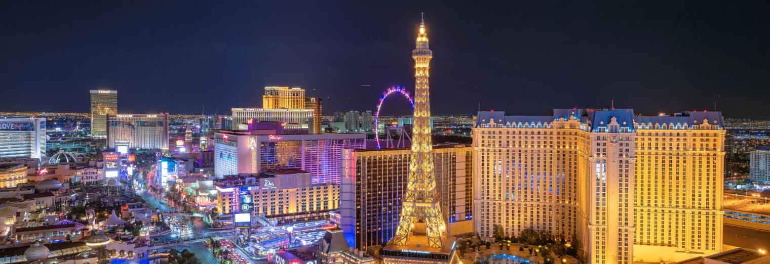 wallypark-airport-parking-fall-deals-inset5 A nighttime view of the Las Vegas Strip, one of the cheap fall travel destinations, featuring brightly lit hotels, casinos, the Eiffel Tower replica at Paris Las Vegas, and the illuminated High Roller observation wheel in the background.