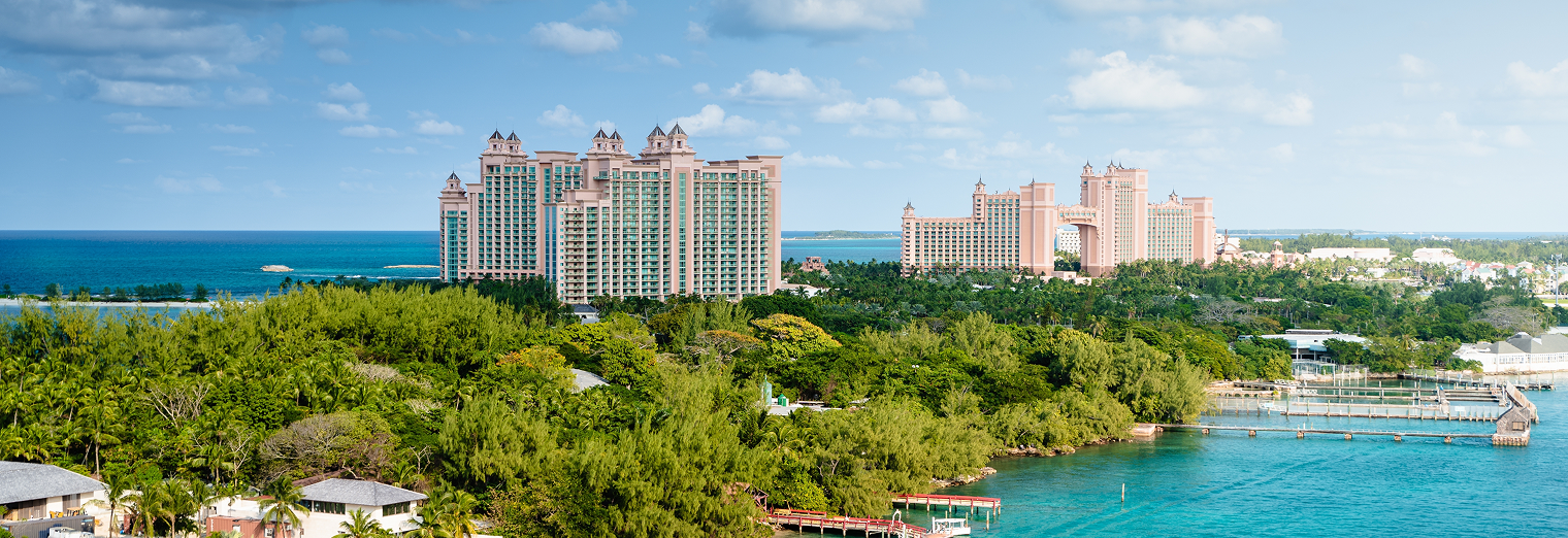 Panoramic view of a lush, green coastline with tall, pink resort buildings in the distance near the blue ocean under a partly cloudy sky—perfect for relaxing after using WallyPark Airport Parking for a smooth travel experience.