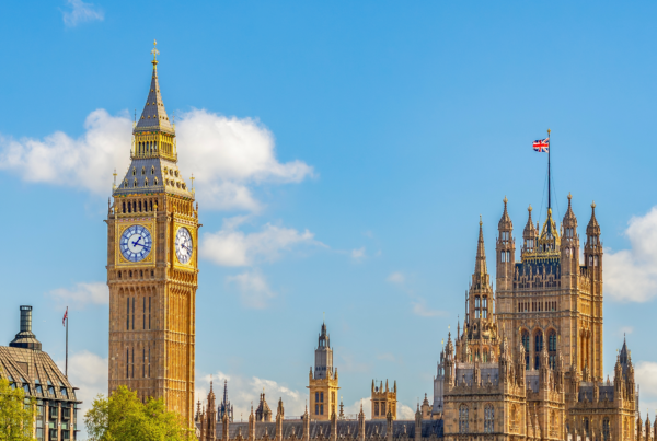 Big Ben and the Houses of Parliament in London, England, stand under a bright blue sky with scattered clouds. The detailed Gothic architecture and Union Jack evoke iconic sights for travelers before heading to WallyPark Airport Parking.